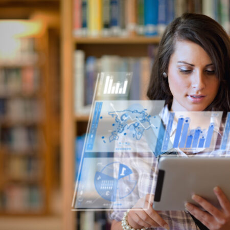 Pretty student working on her futuristic tablet in a library