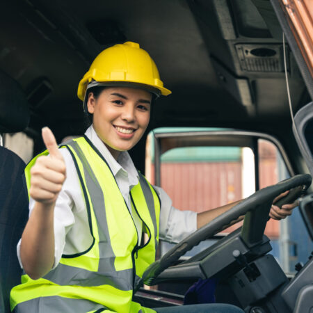 Asian woman truck driver sitting in truck cabin looking at camera.